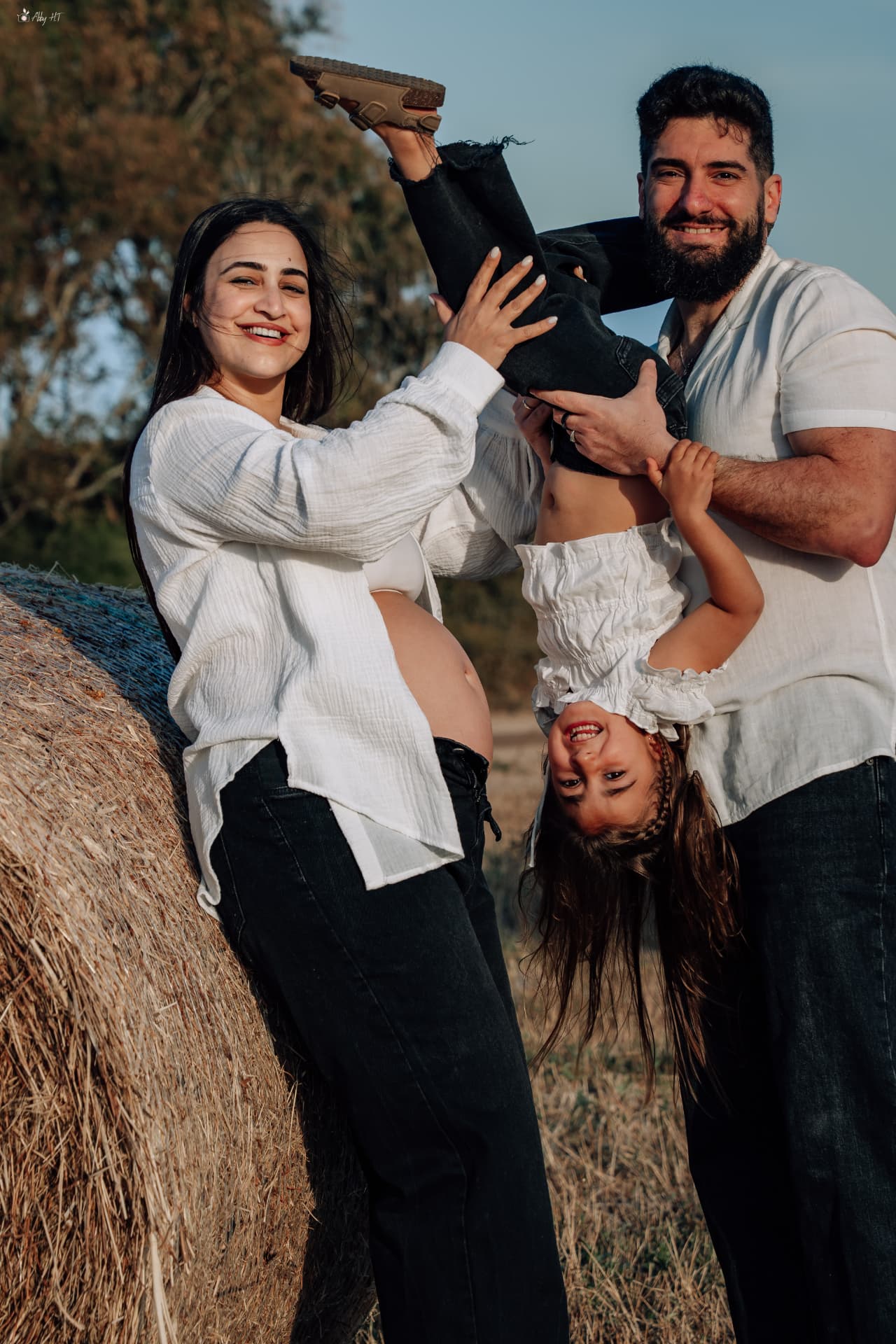 הורים וילדה משחקים ליד ערימת חציר בשעת הזהב