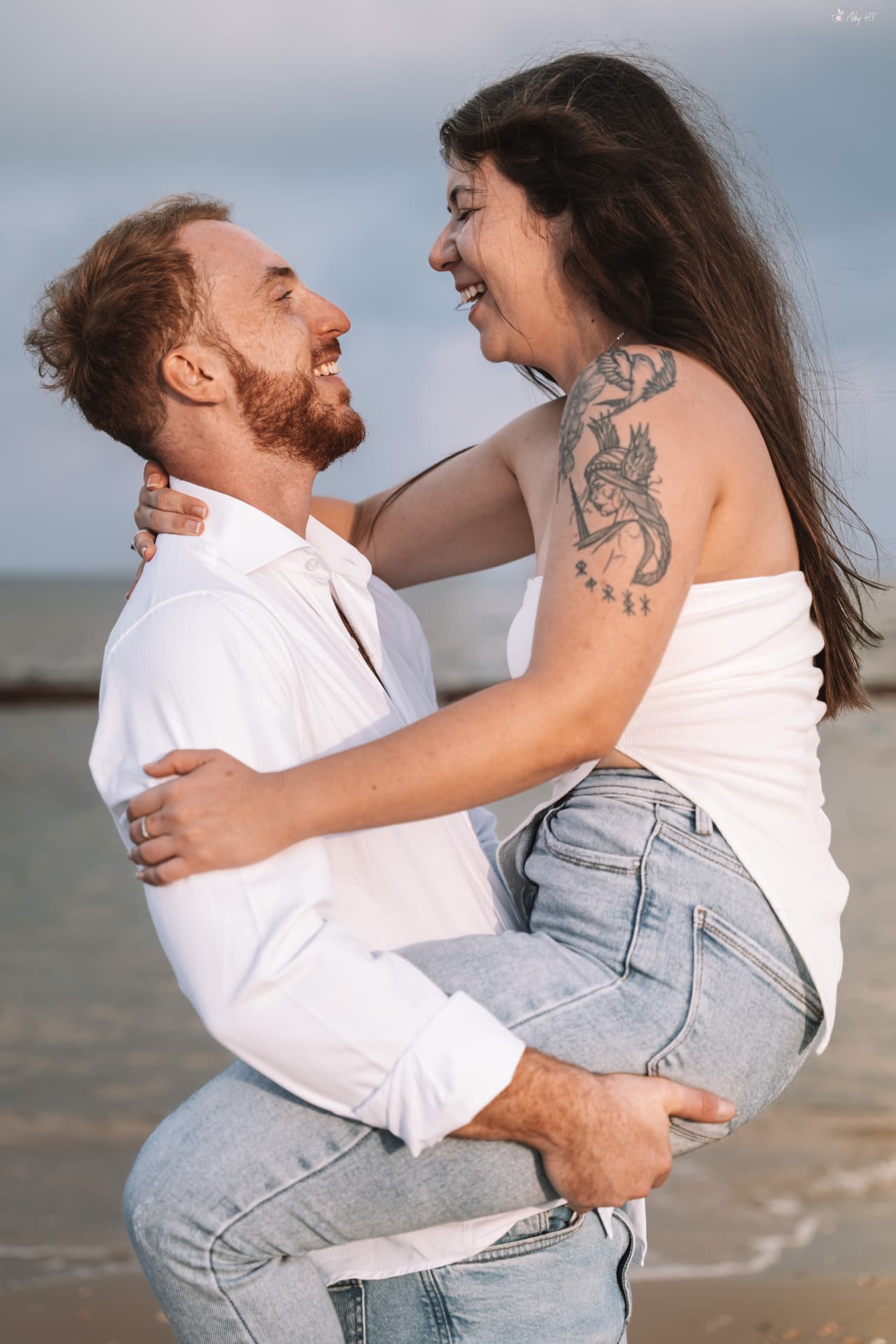 הוא מרים אותה בזרועותיו על החוף, שניהם צוחקים